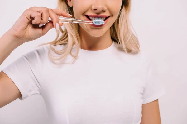 Обрезанный вид женщины в белой футболке, чистящей зубы изолированные на белом — стоковое фото