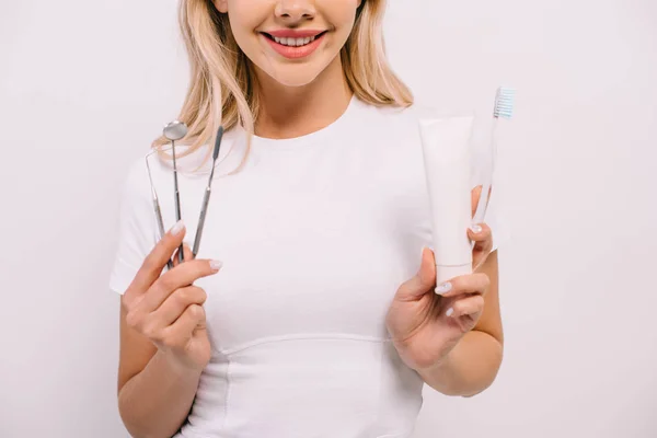 Cropped view of woman holding toothpaste, toothbrush and dental instruments isolated on white — Stock Photo