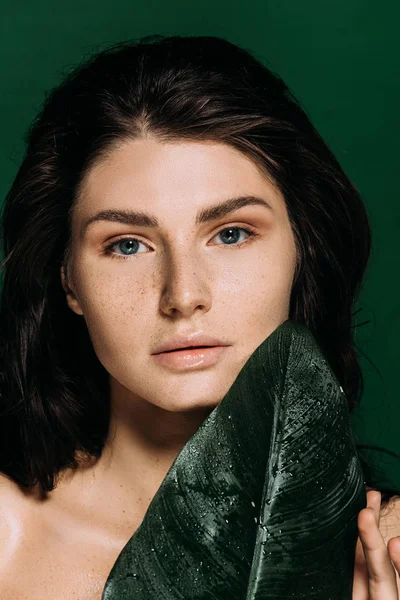 Portrait of brunette woman with freckles on face posing with leaf isolated on green — Stock Photo