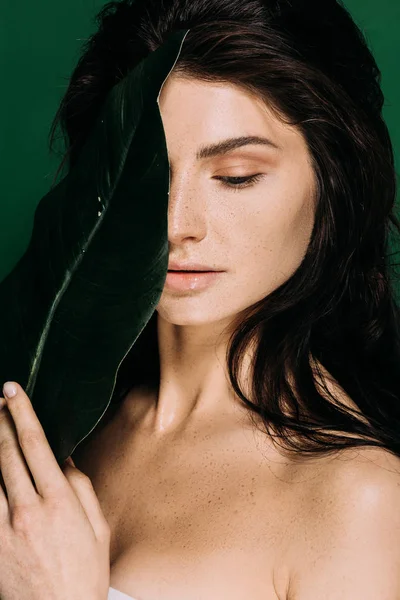 Нежная девушка с веснушками на лице позирует с листом изолированы на зеленый — стоковое фото