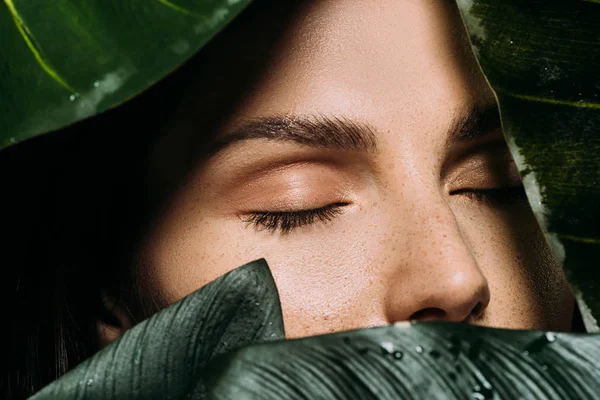 Belle femme aux yeux fermés posant avec des feuilles de palmier vert — Photo de stock