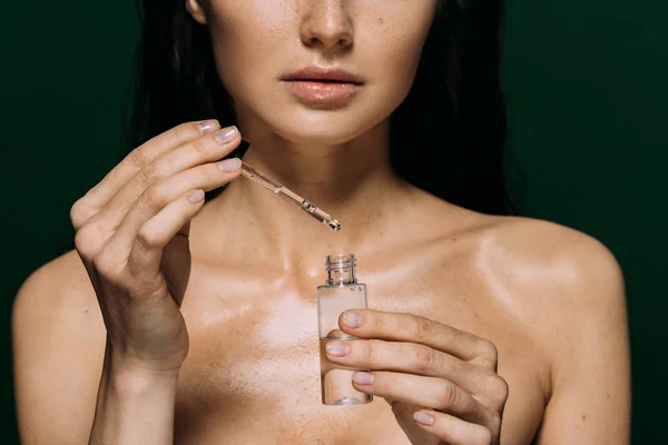 Abgeschnittene Ansicht einer nackten Frau, die eine Flasche mit Serum auf Grün isoliert hält — Stockfoto