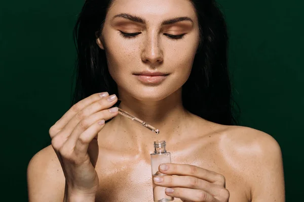 Attractive naked woman holding bottle with moisturizing serum isolated on green — Stock Photo
