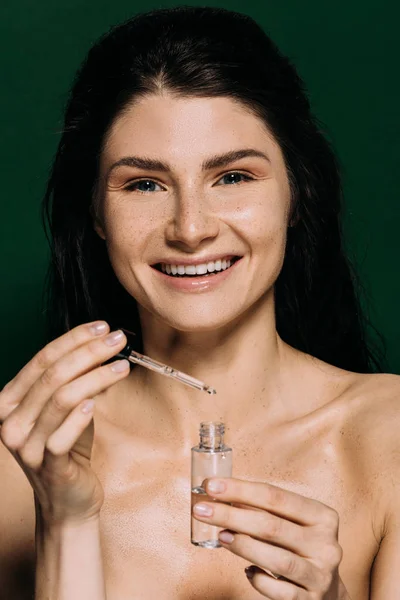 Fröhliche nackte Mädchen halten Flasche mit feuchtigkeitsspendendem Serum isoliert auf grün — Stockfoto