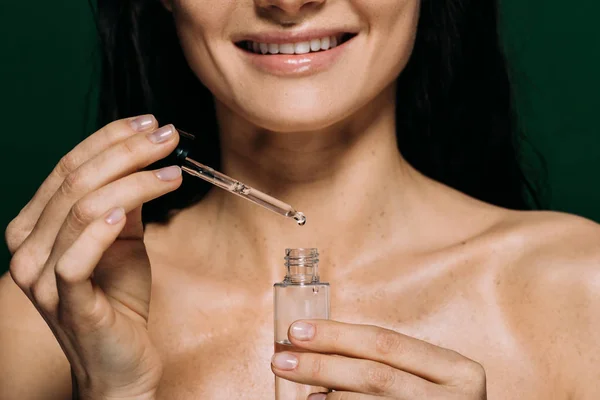 Cropped view of smiling naked woman holding pipette and bottle with serum isolated on green — Stock Photo