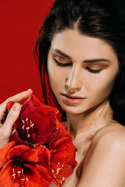 Attraente tenera giovane donna con fiori di amarillide, isolata sul rosso — Foto stock