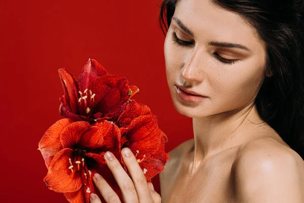 Retrato de jovem mulher concurso olhando para flores amaryllis, isolado em vermelho — Fotografia de Stock