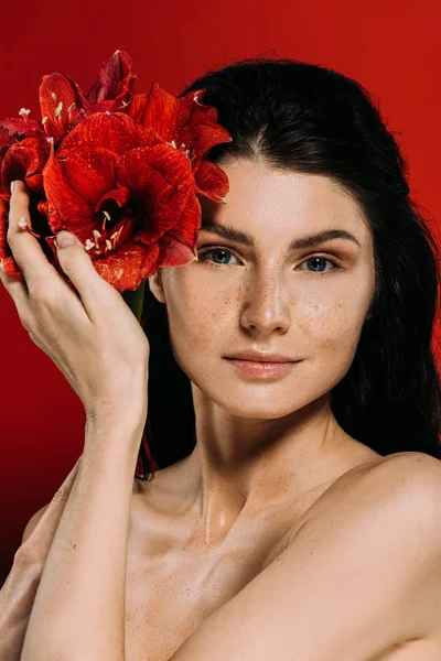 Hermosa mujer con pecas en la cara posando con flores de amarilis, aislado en rojo - foto de stock