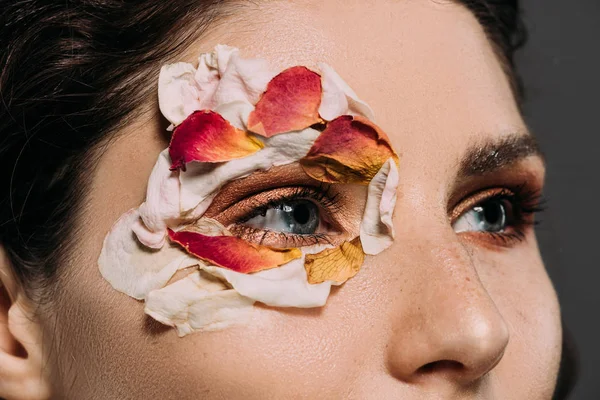 Primer plano de la hermosa mujer con pétalos florales alrededor del ojo aislado en gris - foto de stock