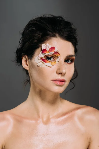 Hermosa joven con pétalos florales alrededor del ojo aislado en gris - foto de stock