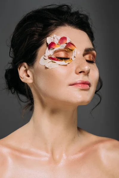 Нежная молодая женщина с закрытыми глазами и лепестками на лице, изолированные на сером — стоковое фото
