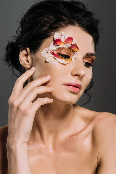 Tierna chica con pétalos florales alrededor de ojo aislado en gris - foto de stock