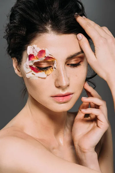Tierna chica morena con pétalos florales alrededor del ojo aislado en gris - foto de stock