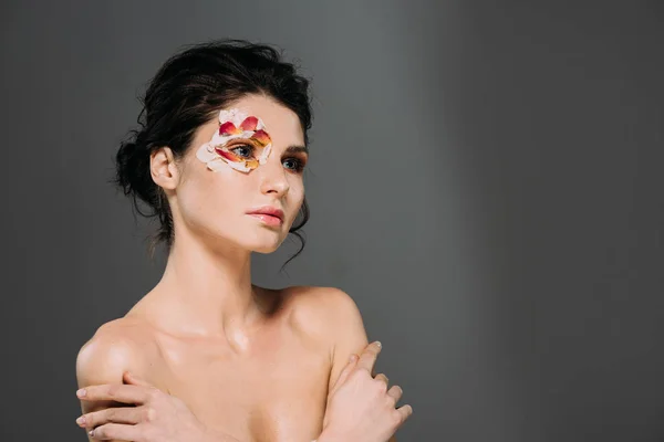 Schöne nackte Frau mit Blütenblättern um Auge isoliert auf grau — Stockfoto