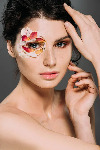 Hermosa mujer desnuda con pétalos florales alrededor del ojo aislado en gris - foto de stock