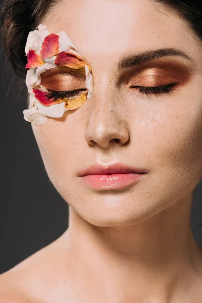Schöne junge Frau mit Blütenblättern und Make-up auf geschlossenen Augen isoliert auf grau — Stockfoto