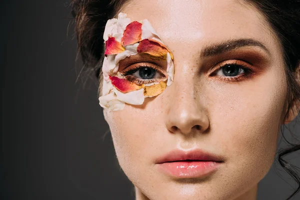 Jolie jeune femme avec maquillage et pétales floraux autour de l'œil isolé sur gris — Photo de stock