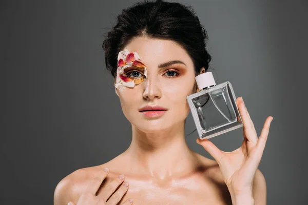 Porträt eines nackten Mädchens mit Blütenblättern im Gesicht mit Parfümflasche isoliert auf grau — Stockfoto