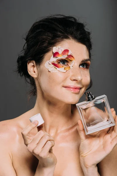 Beautiful naked girl with petals on face smelling perfume isolated on grey — Stock Photo