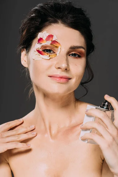 Портрет молодої жінки з пелюстками на обличчі, розпилюючи парфуми ізольовані на сірому — стокове фото