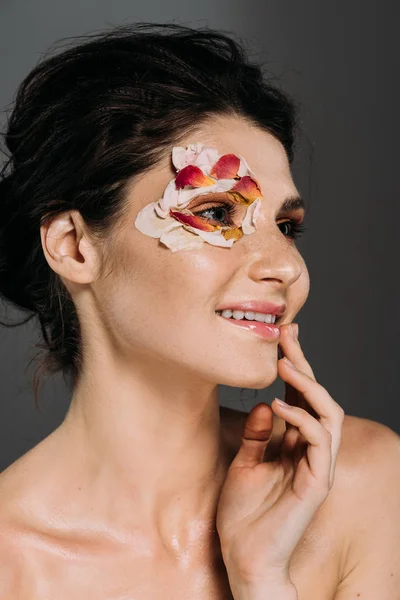 Счастливая брюнетка женщина с лепестками цветов вокруг глаза изолированы на серый — стоковое фото