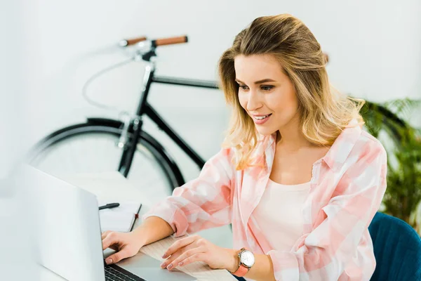 Mujer joven sonriente en reloj de pulsera usando el ordenador portátil en casa - foto de stock