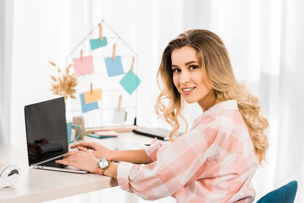 Mulher encaracolado encantador usando laptop com tela em branco no local de trabalho — Fotografia de Stock