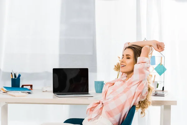 Relaxed young woman in checkered shirt sitting with closed eyes at workplace — Stock Photo