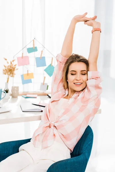 Impresionante mujer joven estirándose con los ojos cerrados en el lugar de trabajo - foto de stock