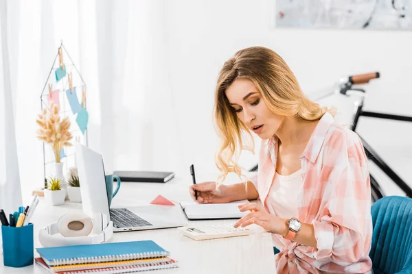Konzentrierte Frau benutzt Taschenrechner und schreibt im Home Office in Notizbuch — Stockfoto
