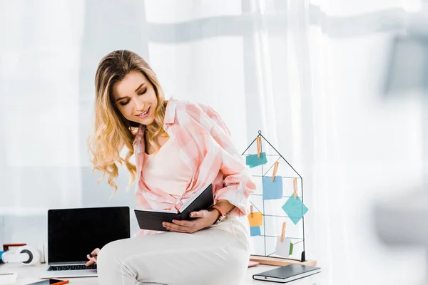 Mulher encaracolada encantadora usando laptop e notas de leitura no local de trabalho — Fotografia de Stock