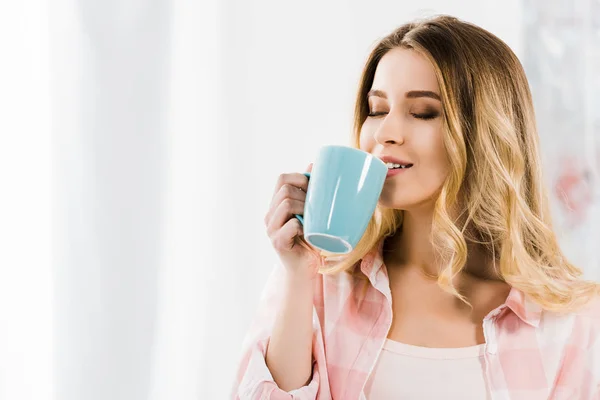 Charming young woman in pink shirt drinking coffee with closed eyes — Stock Photo