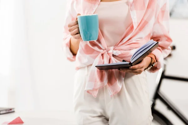 Partial view of woman holding notebook and drinking coffee — Stock Photo