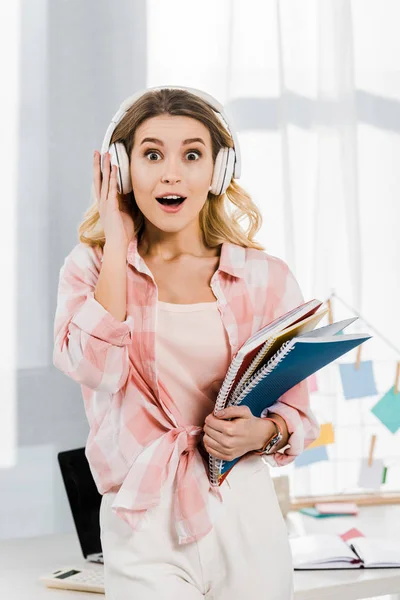 Femme blonde incroyable en chemise à carreaux tenant des carnets et écoutant de la musique — Photo de stock