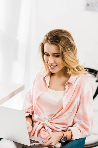Sorridente bella donna in camicia a scacchi utilizzando il computer portatile a casa — Foto stock