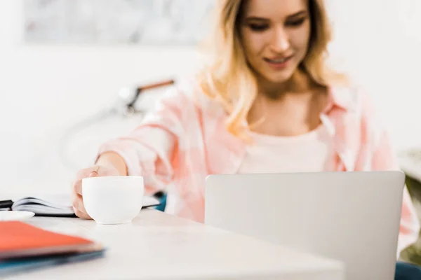 Mujer rubia usando el ordenador portátil y beber café en el lugar de trabajo - foto de stock