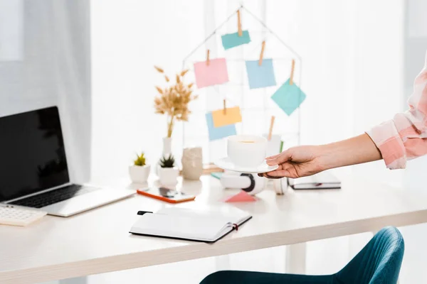 Vista recortada de la mujer sosteniendo la taza de café en el lugar de trabajo - foto de stock