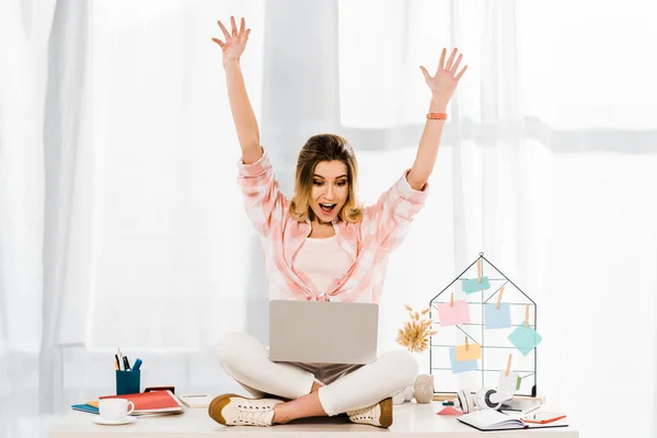 Amazed girl with laptop sitting on table and waving hands — Stock Photo