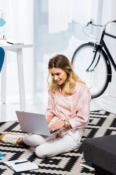Aufgeregtes Mädchen im karierten Hemd auf Teppich sitzend und mit Laptop — Stockfoto
