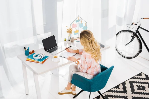 Femme blonde assise sur le lieu de travail et utilisant un ordinateur portable avec écran blanc — Photo de stock