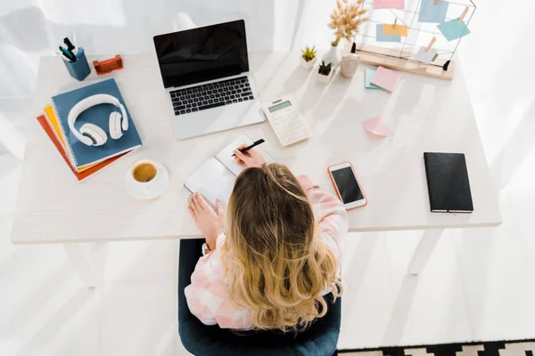 Visão superior da mulher loira escrevendo no notebook no local de trabalho — Fotografia de Stock