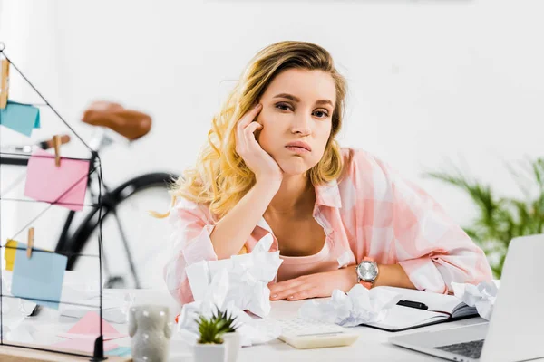 Gelangweilte blonde Frau im karierten Hemd sitzt am Arbeitsplatz — Stockfoto