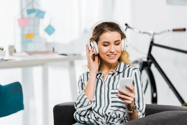 Щаслива молода жінка в смугастій сорочці слухає музику і тримає смартфон — стокове фото