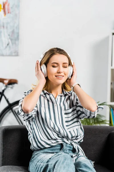 Belle femme en chemise rayée assise sur un canapé et écoutant de la musique — Photo de stock