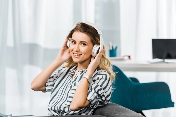 Heureuse femme blonde en chemise rayée écoutant de la musique dans les écouteurs — Photo de stock