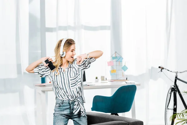 Беззаботная девушка в полосатой рубашке танцует и слушает музыку в наушниках — стоковое фото