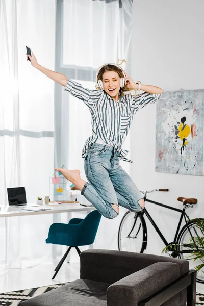 Happy girl in striped shirt jumping and listening music in headphones — Stock Photo