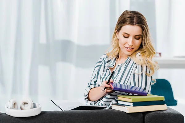 Очаровательная женщина в полосатой рубашке сидит на диване с книгами — стоковое фото