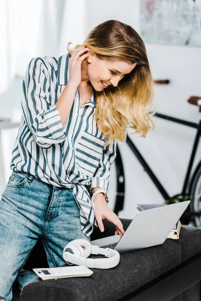 Encantadora joven con camisa a rayas usando el ordenador portátil en casa - foto de stock