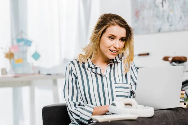 Souriante fille en chemise rayée à l'aide d'un ordinateur portable à la maison — Photo de stock